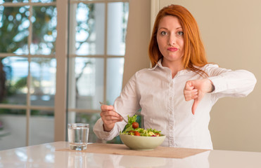 Sticker - Redhead woman eating fresh green salad at home with angry face, negative sign showing dislike with thumbs down, rejection concept