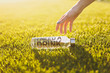 Outstretched hand to bottle with fresh clean clear water with text inscription I need drink on green grass on sunshine lawn. Nature texture background, wallpaper. Soccer field or sports concept design
