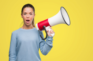 Wall Mural - Beautiful young woman holding megaphone scared in shock with a surprise face, afraid and excited with fear expression