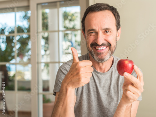 Fotografía Middle age man eating healthy red apple happy with big smile doing ok sign, thum