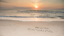 The Words North Carolina Etched In The Sand At Sunrise With Waves Coming Ashore.