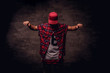 Portrait of an African-American dancer guy dressed in a red fleece shirt and cap at the studio. Isolated on dark textured background.