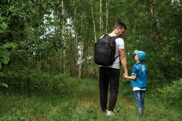 Wall Mural - A man with a backpack, a father and his son on a hike, walking during walks in the woods. Family life, pastime with the family, the upbringing of children.