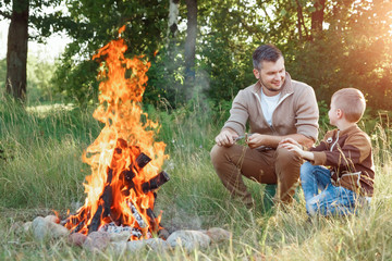 Wall Mural - Father and son by the fire against a background of green nature. Hike, time with family, family life, outdoor recreation.