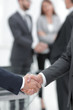 © ASDF - Two businessmen shaking hands with colleagues  on background.