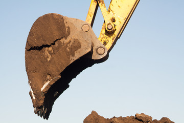 A large iron excavator bucket collects and pours sand rubble and stones in a quarry at the construction site of road facilities