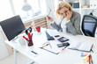 © Ivan Traimak - A young girl is sitting at a table in the office. The girl is holding glasses and rubbing her eyes.
