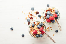 Two Jars With Granola, Berries And Yogurt On White Wooden Table. Top View.