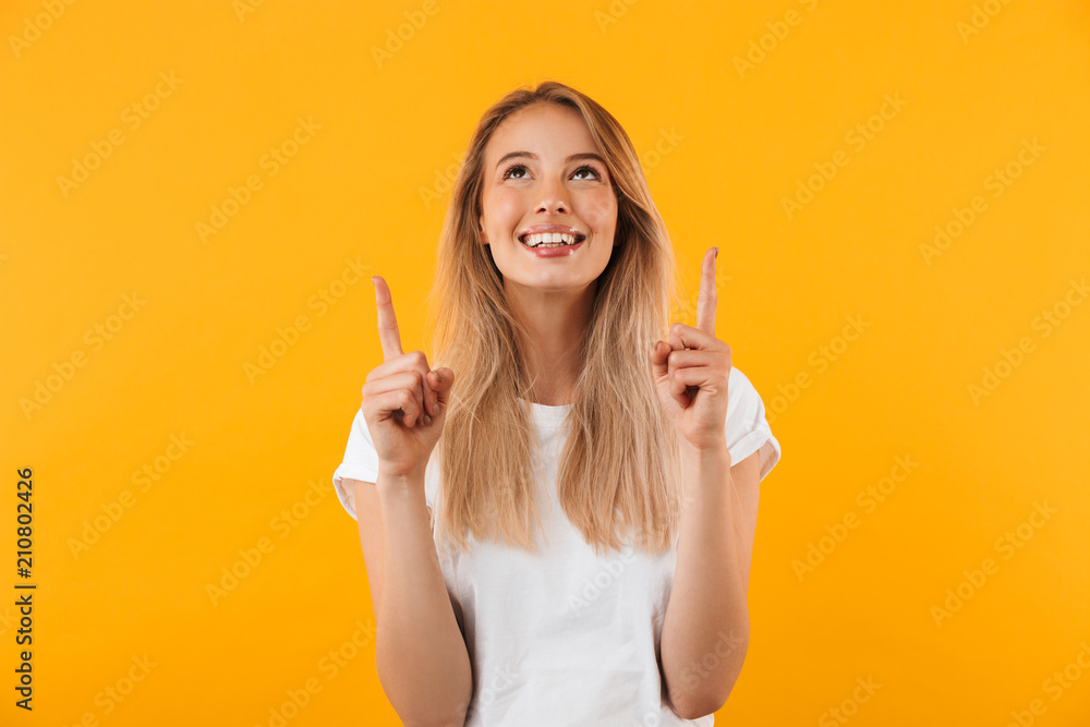 Portrait of a smiling young blonde girl pointing up - obrazy, fototapety, plakaty 