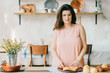 © benevolente - Young beautiful housewife in dress having breakfast on kitchen. Lovely woman posing and dreaming in country french style decorated interior zone. Rustic dining room with fresh food and tableware.