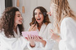 Young smiling women 20s wearing housecoat sitting in luxury bedroom at hotel room, and applying makeup for bride during bridal shower