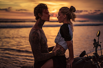 passionate couple hugging on motorcycle at beach during sunset