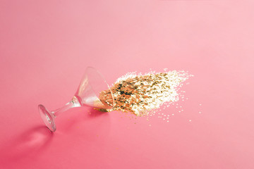 Wall Mural - spilled martini glass full of gold glitter on pink background. creative minimal party concept.