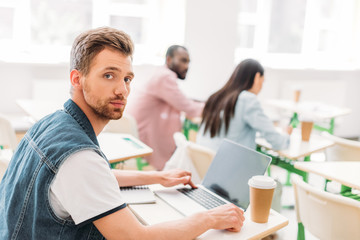 Wall Mural - handsome young student with laptop sitting at classroom