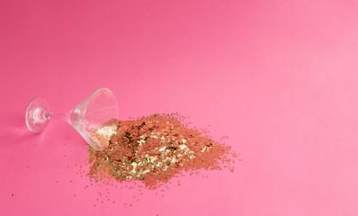 Wall Mural - spilled martini glass full of gold glitter on pink background. creative minimal party concept.
