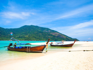 Wall Mural - Wooden long tail boat  in side view at white sand beach with blue sea and mountain in background in sunny summer day at Koh Lipe island,Thailand for vacation holiday concept.