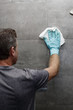 © Serenethos - Man cleaning a gray tile bathroom shower wall with a wet cloth while wearing a protective glove. Gray tile bathroom shower wall being cleaned with a cloth rag by a man wearing a cleaning glove.