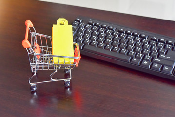 Mini Shopping Cart Filled with Shopping Bag Isolated on Wooden Table with Keyboard as for E-Commerce