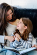 © lordn - Girls having fun at home. Portrait of mother and daughter reading a book