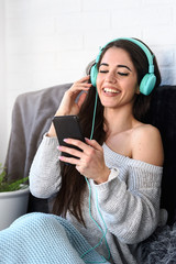 Wall Mural - Portrait of beautiful smiling young woman with headphones indoors listening music