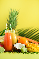 Wall Mural - Juicy papaya and pineapple, mango, orange fruit smoothie in two jars on yellow background. Detox, summer diet food, vegan concept. Copy space. Fresh juice in glass bottles over green palm leaves.