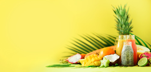 Juicy papaya and pineapple, mango, orange fruit smoothie in jars on yellow background. Detox, summer diet food, vegan concept. Banner. Copy space. Fresh juice in glass bottles over palm leaves.