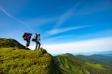 Adventurers with backpacks stands on green mountain ridge