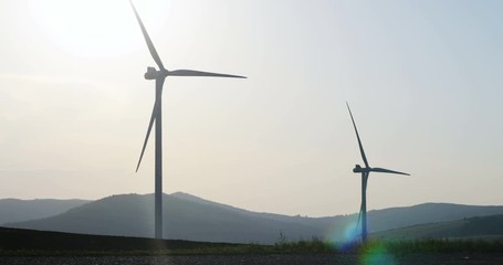 Wall Mural - wind turbines blades rotation slow motion in summer sunny day with bright sun light and mountain area on background clear sky nobody outside converting wind energy electrical engineering equipment