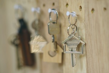 House key with wooden home keyring hanging on wood board background, property concept, copy space