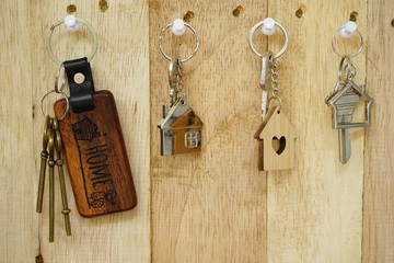 House key with wooden home keyring hanging on wood board background, property concept, copy space