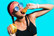 sporty stylish girl in tights, a black top, a bandage on hair, stands on the background of a colored wall. He eats a burger and a piece of fried chicken, drinks soda. Strong emotions, smile, fast food