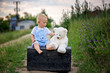 © Tomsickova - Cute toddler boy, sitting on vintage suitcase, playing with teddy bear on rural path
