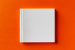 Mockup of square white closed book with leather cover isolated at orange design paper background.