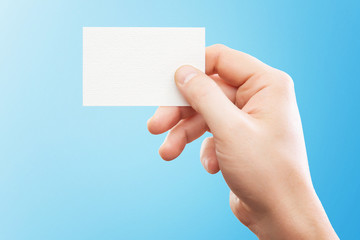 Wall Mural - Male hand holding white business card at isolated blue background mockup.