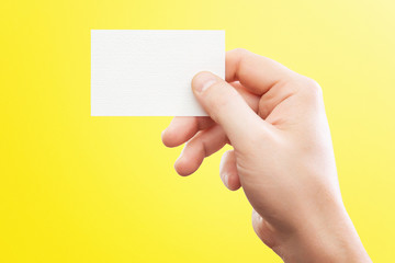 Wall Mural - Male hand holding white business card at isolated yellow background mockup.