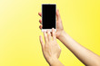 © Mayatnikstudio - Mockup of female hands holding modern white cellphone with black screen and making sliding gesture isolated at yellow background.