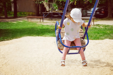 Little baby girl caucasian appearance sitting on a swing and laughing