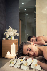 Young couple relaxing under the stimulating effects of a traditional hot stone massage at luxury spa and wellness center