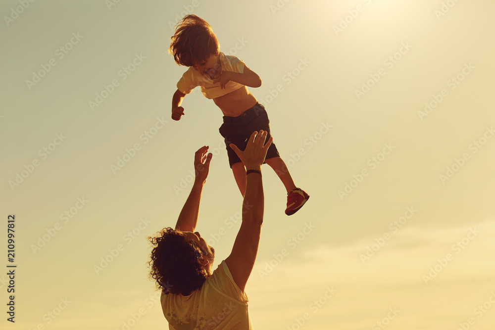 Father and child playing in nature at sunset. Dad throws his son in the ...