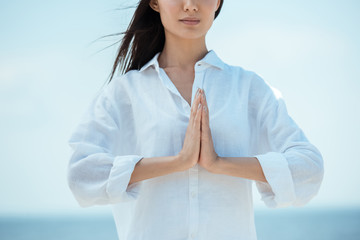 Wall Mural - cropped image of asian woman doing namaste mudra gesture on beach