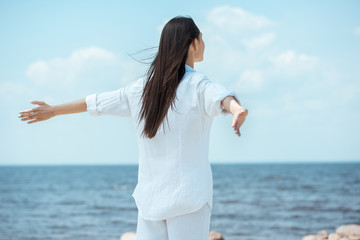 Wall Mural - rear view of woman standing with arms outstretched by sea