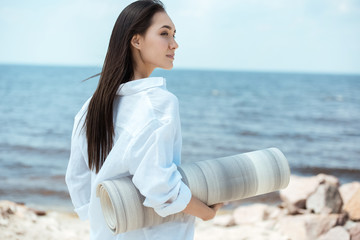 Wall Mural - side view of asian young woman holding yoga mat on beach