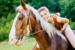 Portrait of happy smiling woman cowgirl, riding a brown horse. Clothed white jeans shorts, brown leather vest. Has slim sport body. Portrait nature. People and animals concept.
