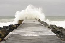 A Wave Crashes Over The End Of A Pier In Windy Conditions