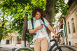 © iuricazac - Handsome happy young male student with curly hair wearing shirt with backpack, sitting on the bicycle on the street, browsing on social media on mobile phone, having joyful look, preparing for college