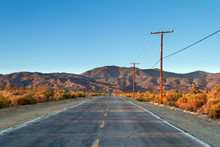 Single Country Road In The Mojave Desert Facing Mountains In A Early Morning Drive.