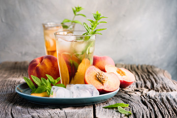 Wall Mural - Refreshing iced tea with ripe peaches on rustic background, selective focus, toned image