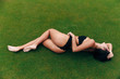 Beautiful young girl with sexy figure posing lying on green grass in a golf park. The model is dressed in a black trendy swimsuit, gently pulls the panties up, bent the leg in the knee from above