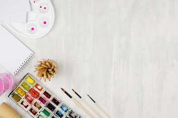 Stationery for painters - paints, palette, brushes, colored pencils, sketchbook on white wooden background, top view, copy space.