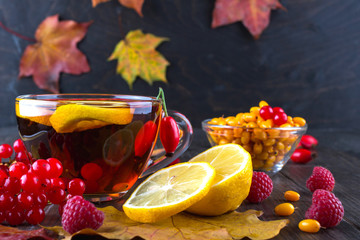 Autumn healthy beverages concept. Cup of tea with autumn berries sea buckthorn,  viburnum, rose hip, rowan and fall leaves. Drink with vitamin c